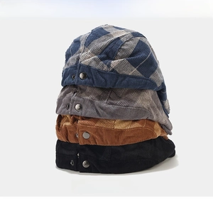 Close-up of stacked corduroy beret hats in plaid, grey, and brown with metal buckles