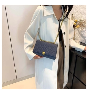 Detail of dark blue denim crossbody bag featuring diamond quilting and gold chain strap