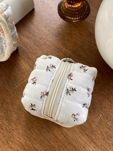 Quilted floral data cable storage bag with pink flowers and a metal clip on wooden desk