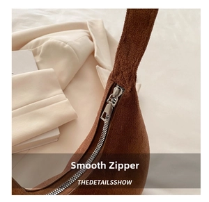 Detail view of smooth silver zipper on a brown suede baguette bag with warm lighting