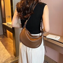 Dettaglio di una borsa a tracolla a mezzaluna in pelle marrone indossata da modella