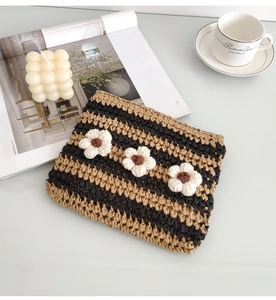 Detail of hand-woven striped straw clutch with handmade crochet white flowers on top