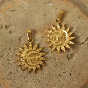 Macro view of gold-plated sun and moon face pendants on a natural stone surface