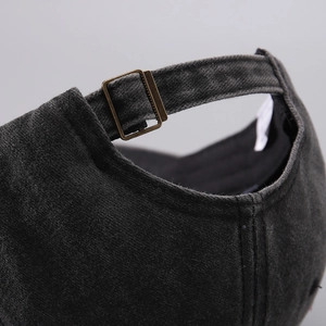 Detail of adjustable bronze metal buckle on washed dark grey cotton baseball cap