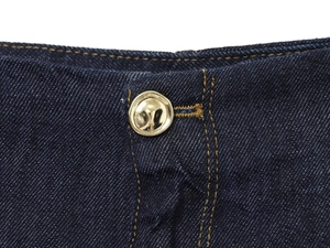 Détail du tissu denim bleu foncé avec un bouton en métal doré poli et couture jaune