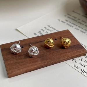 Primer plano de pendientes de nudo en oro y plata sobre un soporte de madera
