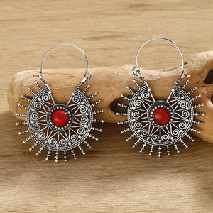 Close-up of silver boho earrings with intricate filigree and red stones on wood