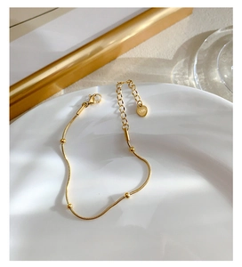 Detailed close-up of 18K gold bracelet with heart charm and lobster clasp on white plate