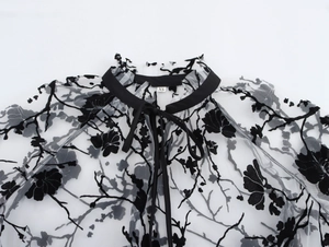 Detail of sheer black floral flocked mesh top with ruffle collar and ribbon tie closure