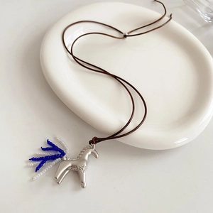 Détail d'un pendentif cheval argenté avec pompon de perles bleues sur cordon brun