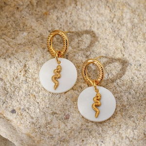 Detail of gold snake earrings with white shell pendants on a natural stone surface