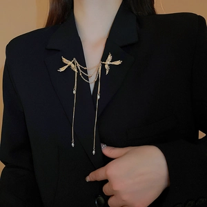 Dettaglio della spilla dorata a due uccelli con nappe di perle su blazer nero