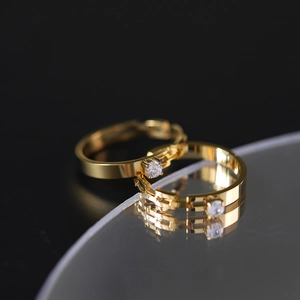 Close-up of elegant pair of gold rings with single round diamond on dark reflective surface