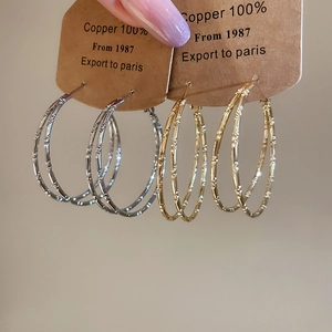 Macro detail of large gold and silver bamboo texture hoop earrings on a copper display card