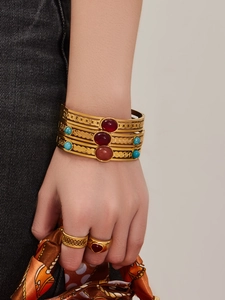 Close-up of gold geometric bangles and rings set with turquoise and red stones