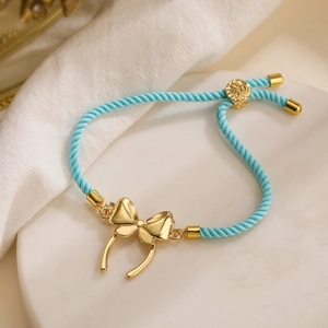 Close-up of light blue woven bracelet with gold bow charm and adjustable metallic ends