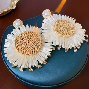 Detailed shot of woven daisy earrings with pearls and crystal pendants on a green stand
