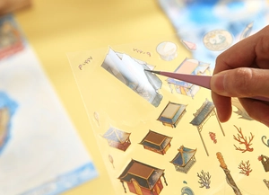 Detail of hand using tweezers to apply Chinese style 3D PET palace and coral stickers