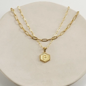 Close-up of gold double-layer necklace with hexagonal pendant featuring embossed letter P