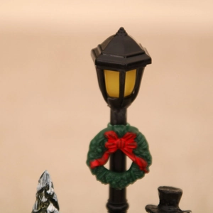 Close-up of a miniature black Christmas street lamp with warm light and festive wreath