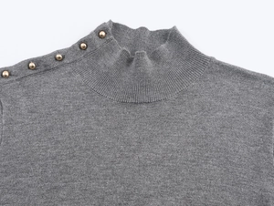 Detail of grey mock neck knit sweater with decorative gold buttons on the shoulder
