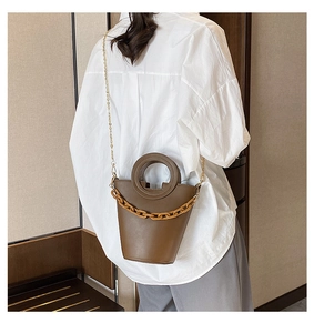 Detail of a dark brown bucket bag with round handle and resin chain on a model