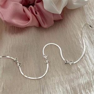 Detail of silver snake chain necklace with three small bow charms on silk fabric