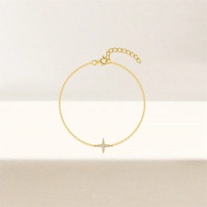 Detail of a thin gold chain bracelet with a sparkling four-pointed star pendant and lobster clasp