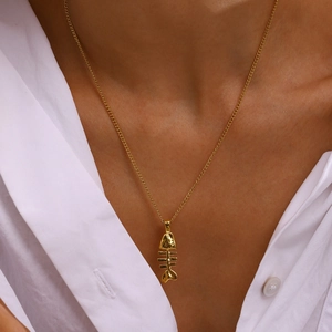 Gros plan d'un collier pendentif arête de poisson doré porté par un mannequin en blanc