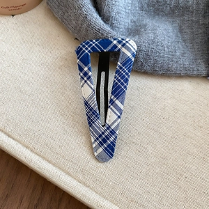 Detail of blue and white plaid fabric triangle hair clip on beige canvas background