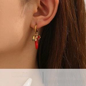 Detail of gold hoop earring featuring a red chili pendant and iridescent butterfly charm