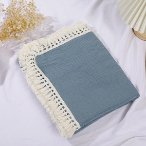 Close-up of a blue cotton waffle baby blanket with decorative cream white fringe tassels