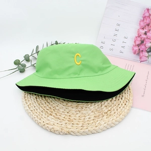 Detail of green double-sided bucket hat with yellow embroidered C on woven mat