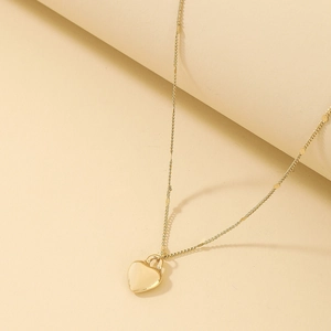 Detailed macro view of a gold heart pendant necklace on a minimalist warm-toned background