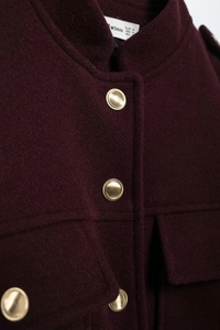 Dettaglio del cappotto di lana bordeaux con tessuto strutturato e bottoni dorati