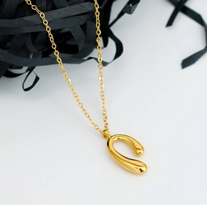 Macro shot of polished gold horseshoe U-shaped pendant necklace on white background