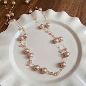 Long champagne pearl and crystal necklace with gold plating shown on ceramic plate