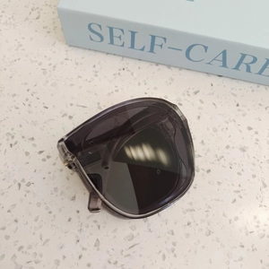 Folded kids' dark grey transparent sunglasses with UV protection on a textured surface