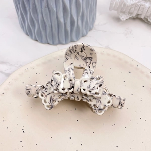 Detail of a creamy white acetate hair claw with elegant black marble ink patterns