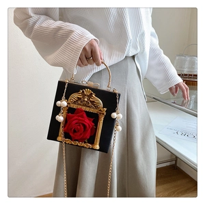 Close-up of black retro handbag with golden frame, red rose detail and pearl tassels