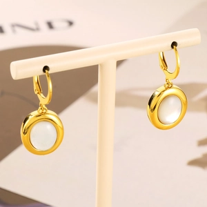 Detail of gold hoop earrings with white opal stone on a beige jewelry display stand