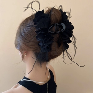 Detail of elegant black fabric flower hair claw with feathers worn by a model
