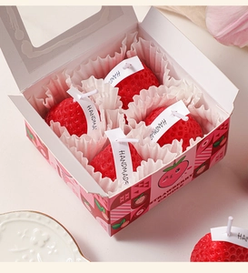 Close-up of four red strawberry-shaped candles in a pink decorative gift box