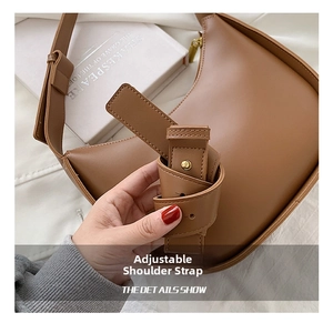 Détail de la bandoulière large réglable avec boucle dorée sur un sac selle marron caramel