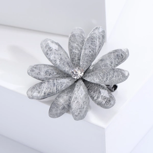 Detailed close-up of a silver-gray acrylic flower brooch with central crystal on white base