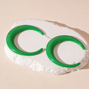 Detailed view of large green acrylic C-shaped earrings on an artistic stone base
