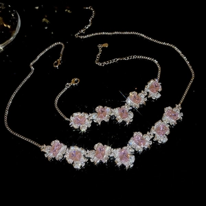 Detailed view of silver necklace and bracelet set with pink square zircon stones on black back