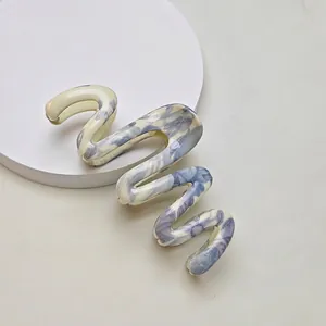 Detail of S-shaped hair claw clip with blue marble ink pattern on a minimalist stand