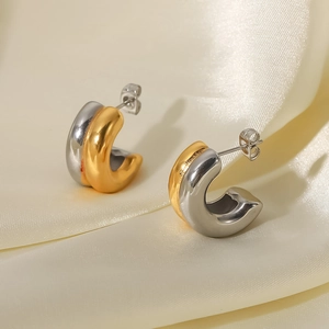 Detail von zweifarbigen C-förmigen Edelstahl-Ohrringen in Gold und Silber auf Seide