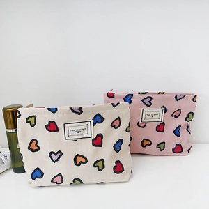 Vista dettagliata della trousse in tela con stampa a cuori colorati e etichetta tessuta sul tavolo.